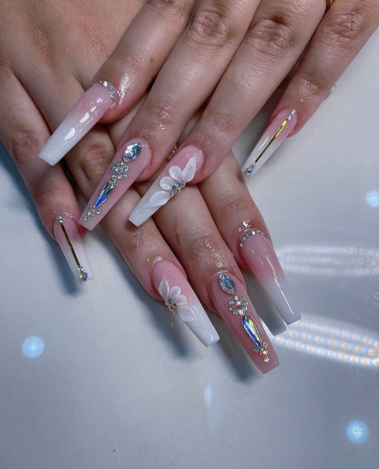 Pink ombre coffin nails with 3D white floral designs and gem embellishments